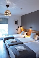 A hotel room with two beds, a wooden headboard, a large window with blinds, a hanging light fixture, and a framed picture on the wall.