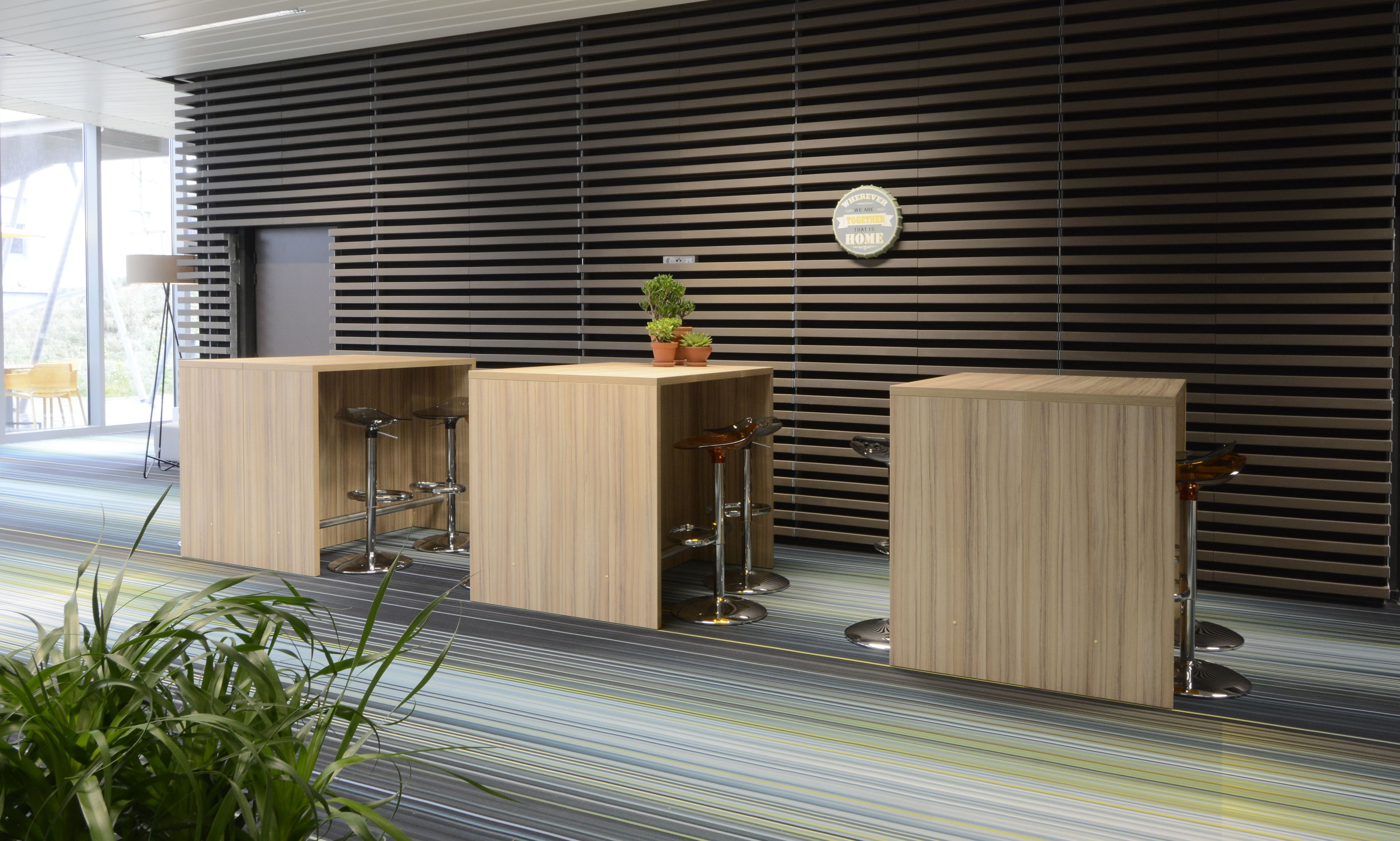A reception area with three wooden counters, each with a glass top and metal base. There is a potted plant on the central counter.