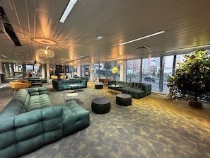 A spacious lounge area with multiple seating options, large windows offering views of the city, and modern lighting fixtures.