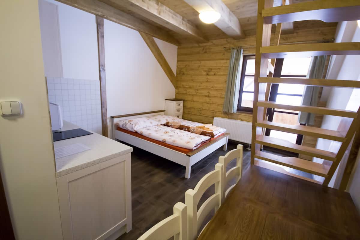 A bedroom with a wooden ceiling, a bed with a white headboard, a small bedside table, and a window with curtains.