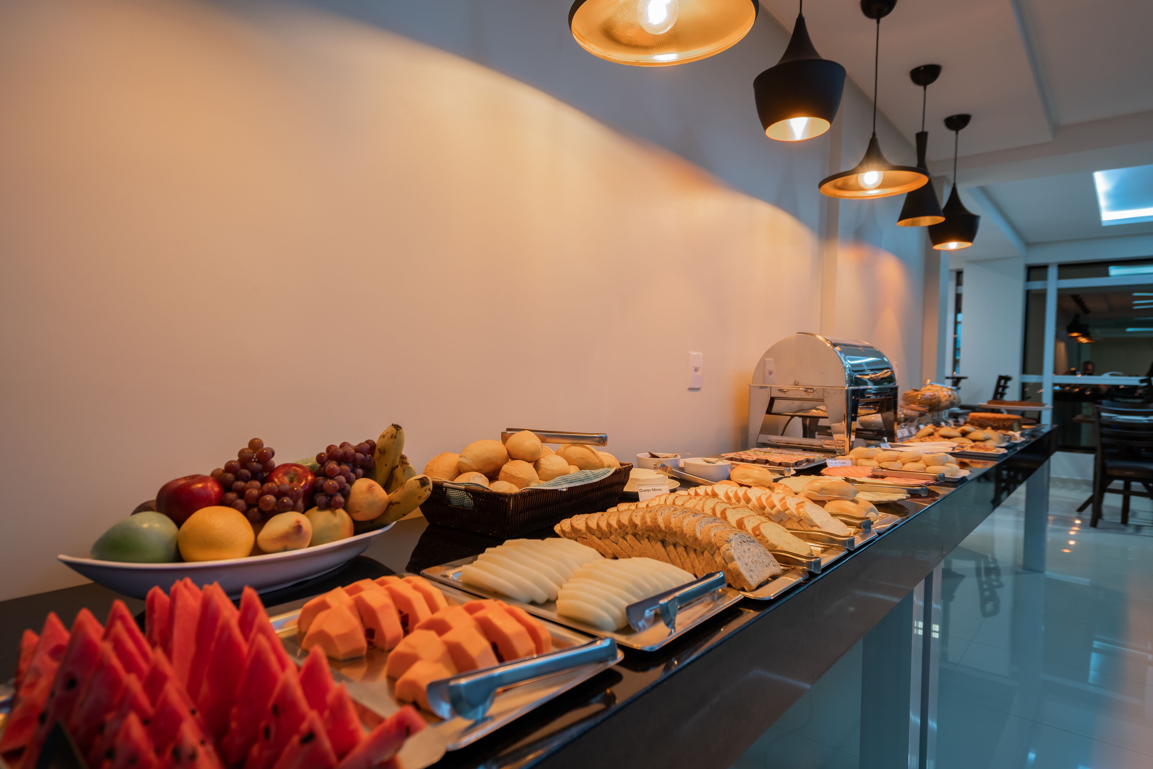 A buffet with various food items including fruits, bread, and pastries.