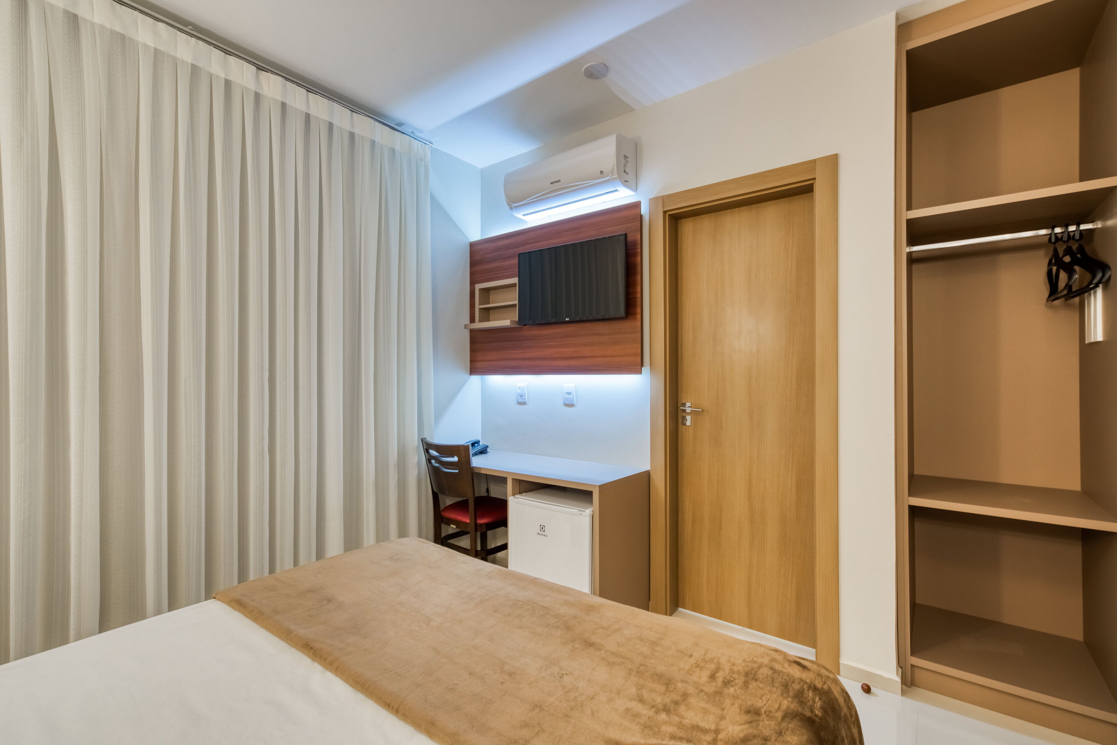 Un dormitorio con cama, escritorio, silla, armario y aire acondicionado.