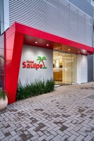 Entrada de hotel con fachada roja y blanca, logotipo de palmera y puerta de cristal.