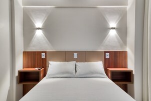 Una habitación de hotel moderna con una cama grande, cabecero de madera, mesitas de noche e iluminación en la pared.