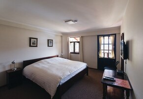 Quarto com cama grande, escrivaninha, cadeira, televisão e duas imagens emolduradas na parede.