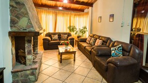 Una sala de estar acogedora con chimenea de piedra, sofás de cuero y piso de baldosas.