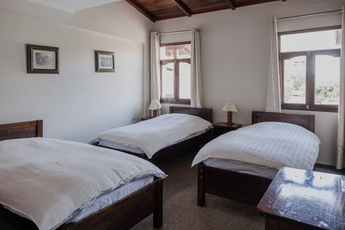 A room with two single beds, a wooden table, and a window with curtains.