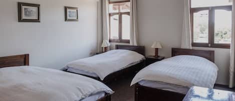 Una habitación con dos camas individuales, una mesa de madera y una ventana con cortinas.