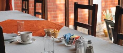 A dining table set with plates, cutlery, a cup, and a glass, with a brick wall and windows in the background.