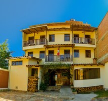 Um edifício de dois andares com varanda em cada andar, uma bandeira e uma escadaria de pedra que leva à entrada.