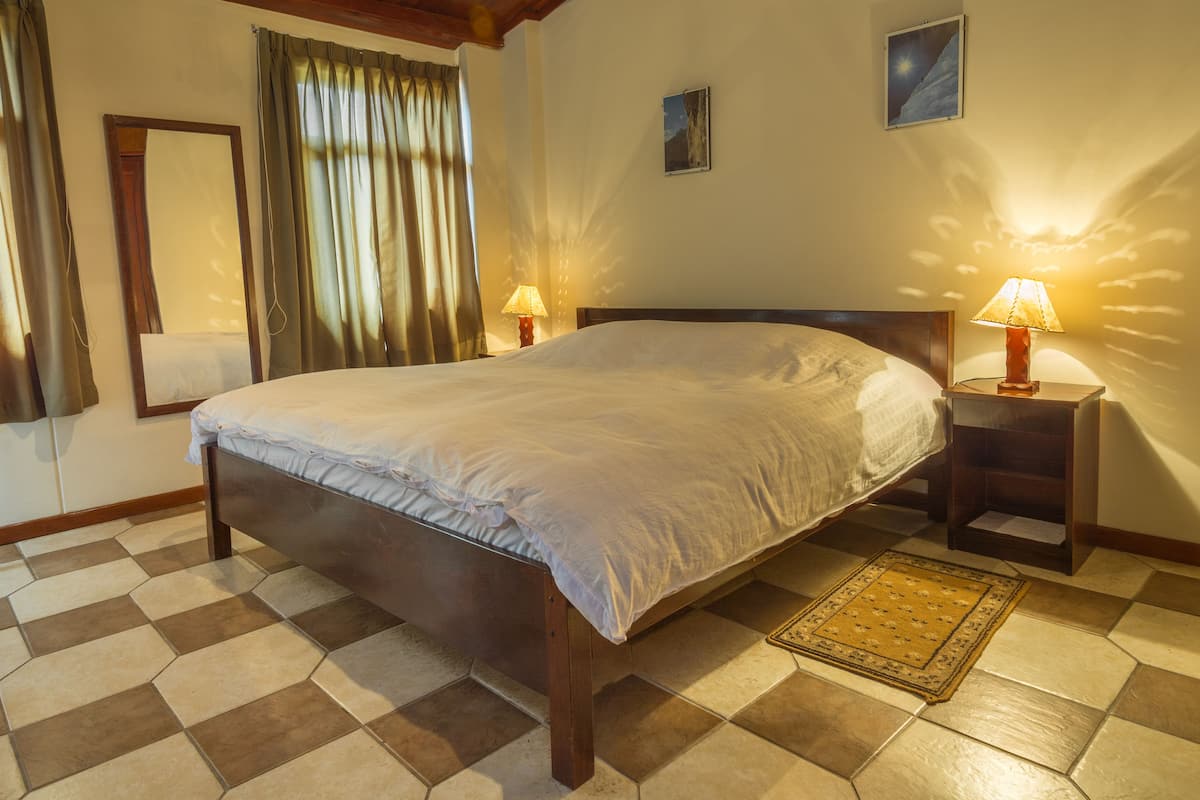 A bedroom with a large bed, two bedside tables with lamps, a mirror, and a checkered floor.