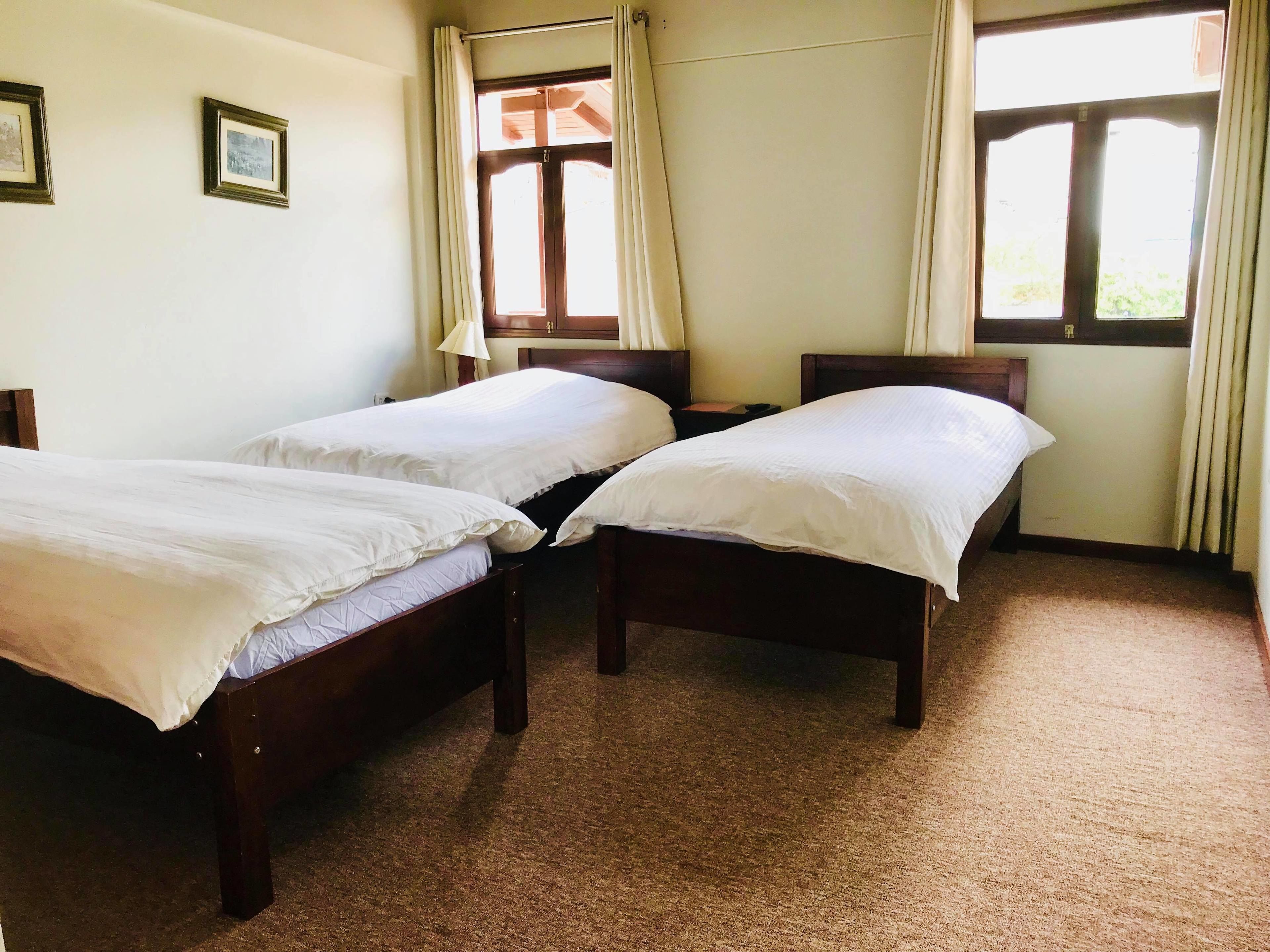 A room with two wooden beds, a window with curtains, and a wall-mounted lamp.