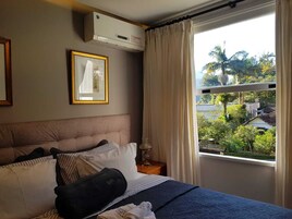 Habitación de hotel con cama, un cuadro en la pared, equipo de aire acondicionado y ventana con cortinas.