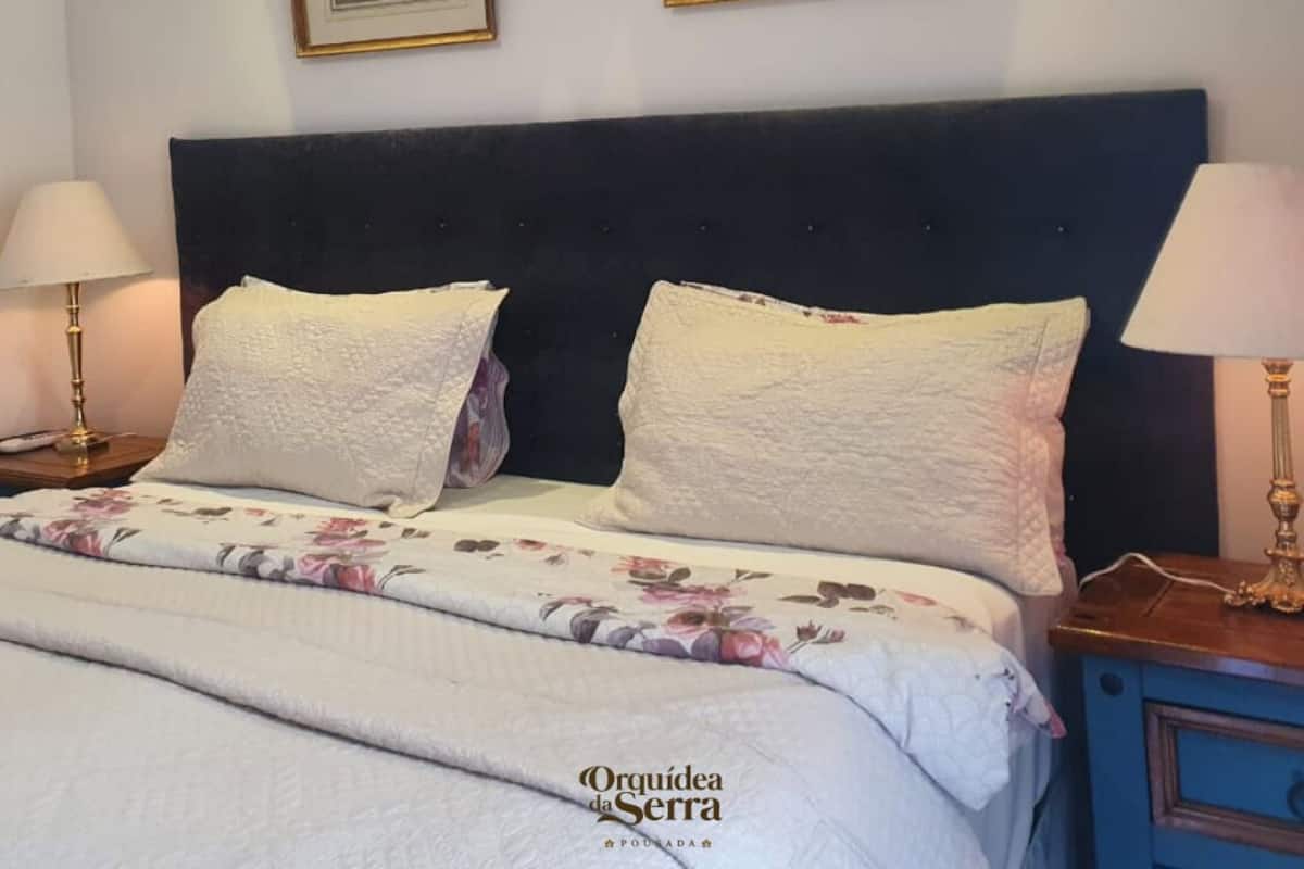 A bedroom with a dark headboard, two framed pictures on the wall, a bed with floral bedding, and two bedside lamps.