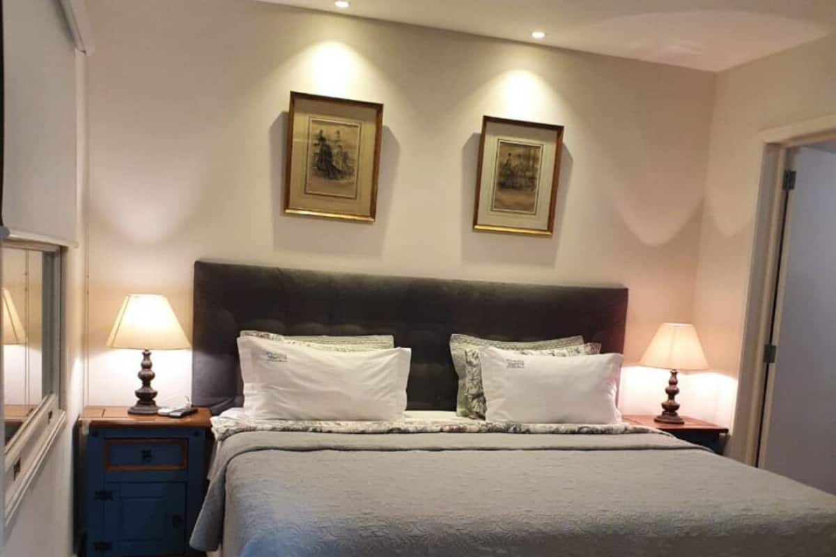 A bedroom with a large bed, two bedside tables with lamps, and two framed pictures on the wall.