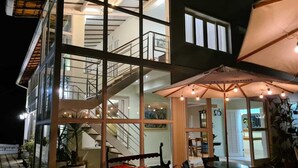 A modern multi-story building with a glass facade, outdoor seating area, and a staircase leading to an upper level. - Pousada Orquídea da Serra (Petrópolis)