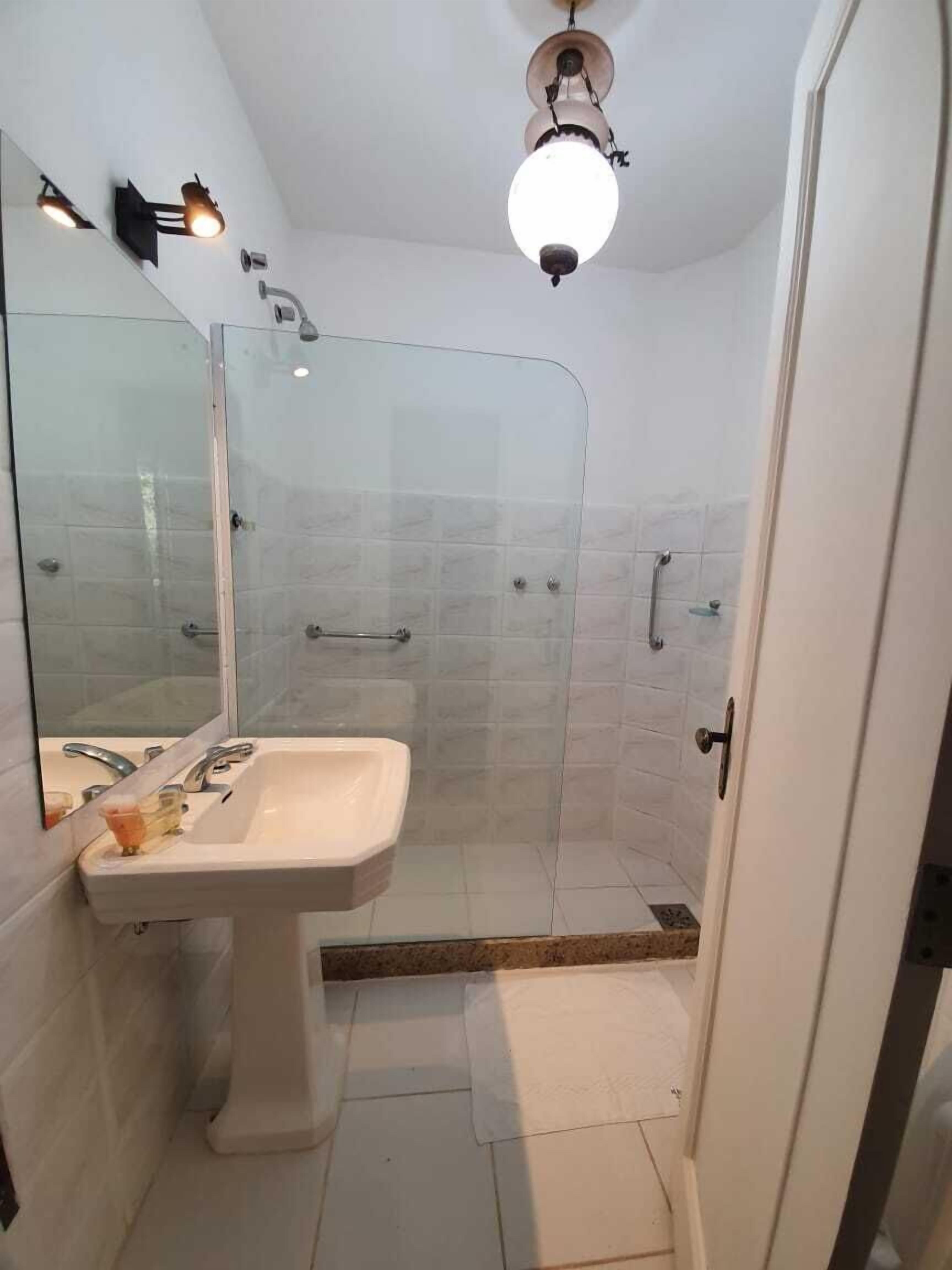 Un baño con ducha de mampara de vidrio, lavamanos pedestal y espejo.