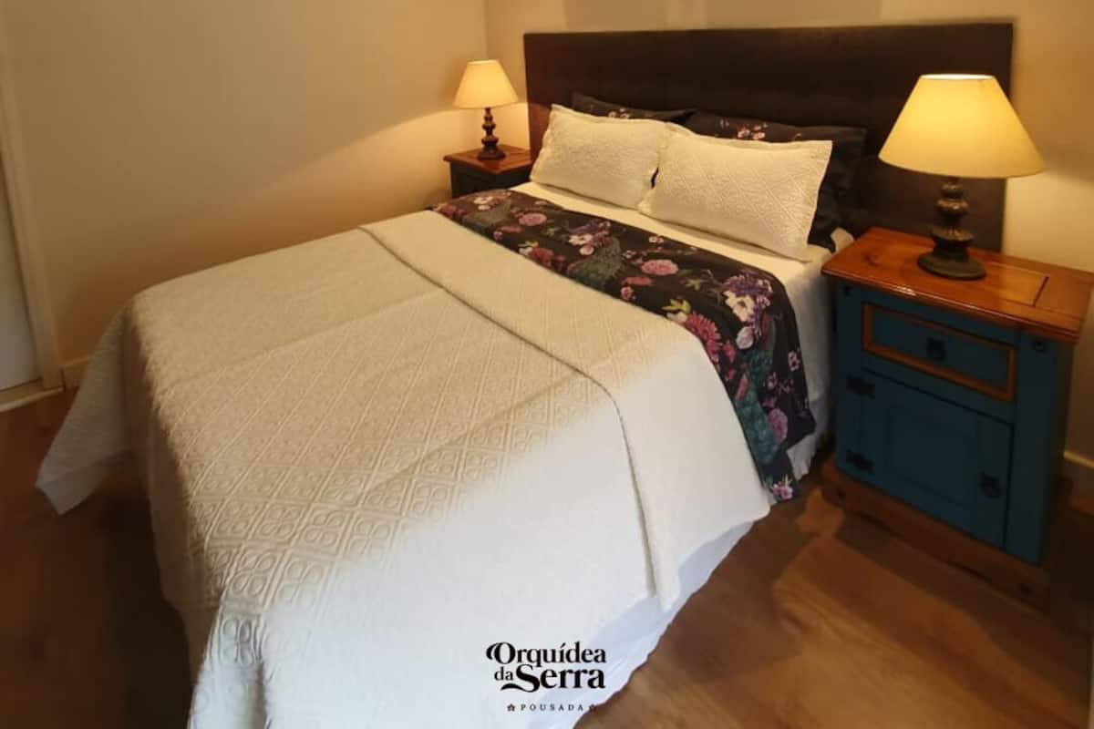 A neatly made bed with a floral bedspread, two bedside tables with lamps, and a wall-mounted air conditioner.
