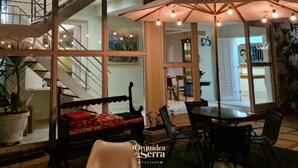 An outdoor patio area with a dining table, chairs, and a bench. There is a staircase leading to an upper level, and a large umbrella providing shade. - Pousada Orquídea da Serra (Petrópolis)