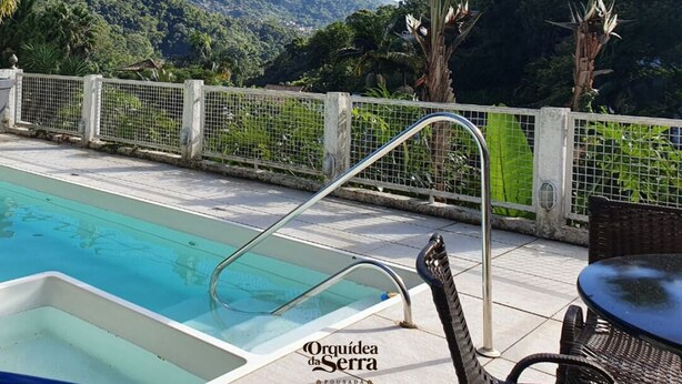 A pool area with a view of mountains, a covered seating area, and a sign reading "Orquidea da Serra." - Pousada Orquídea da Serra (Petrópolis)