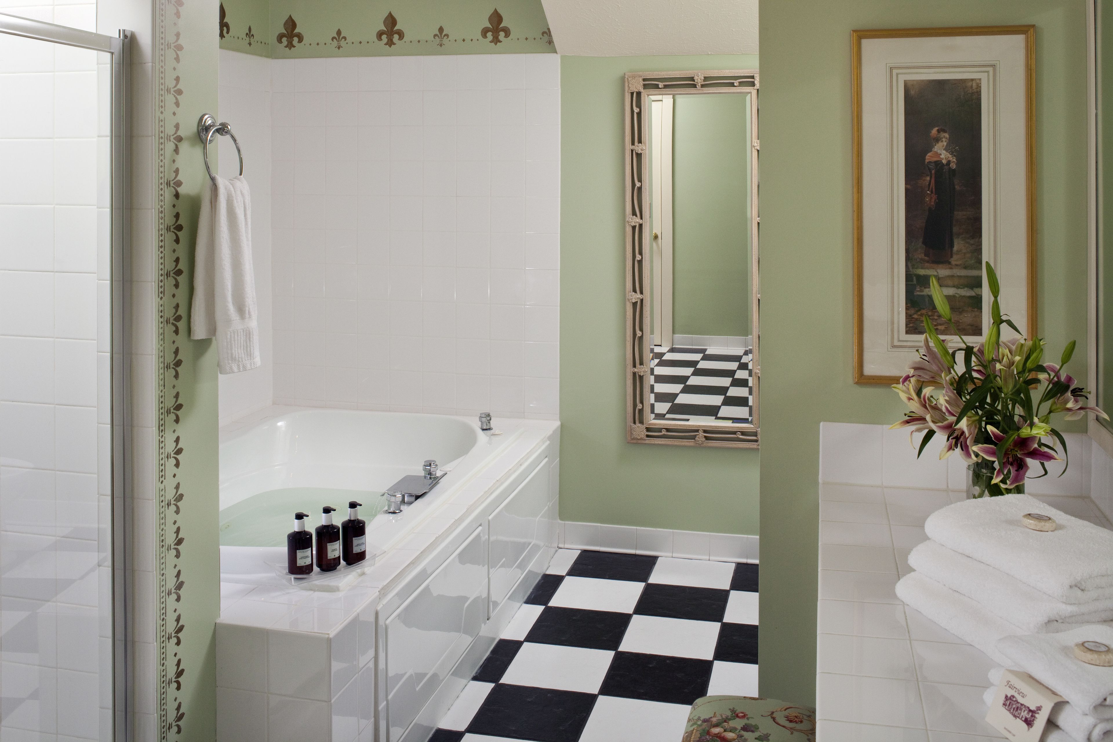 A bathroom with a white bathtub, a checkered floor, and a mirror with a black and white frame.