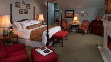 A four-poster bed with a red upholstered bench, a red armchair, and a small table with a lamp.