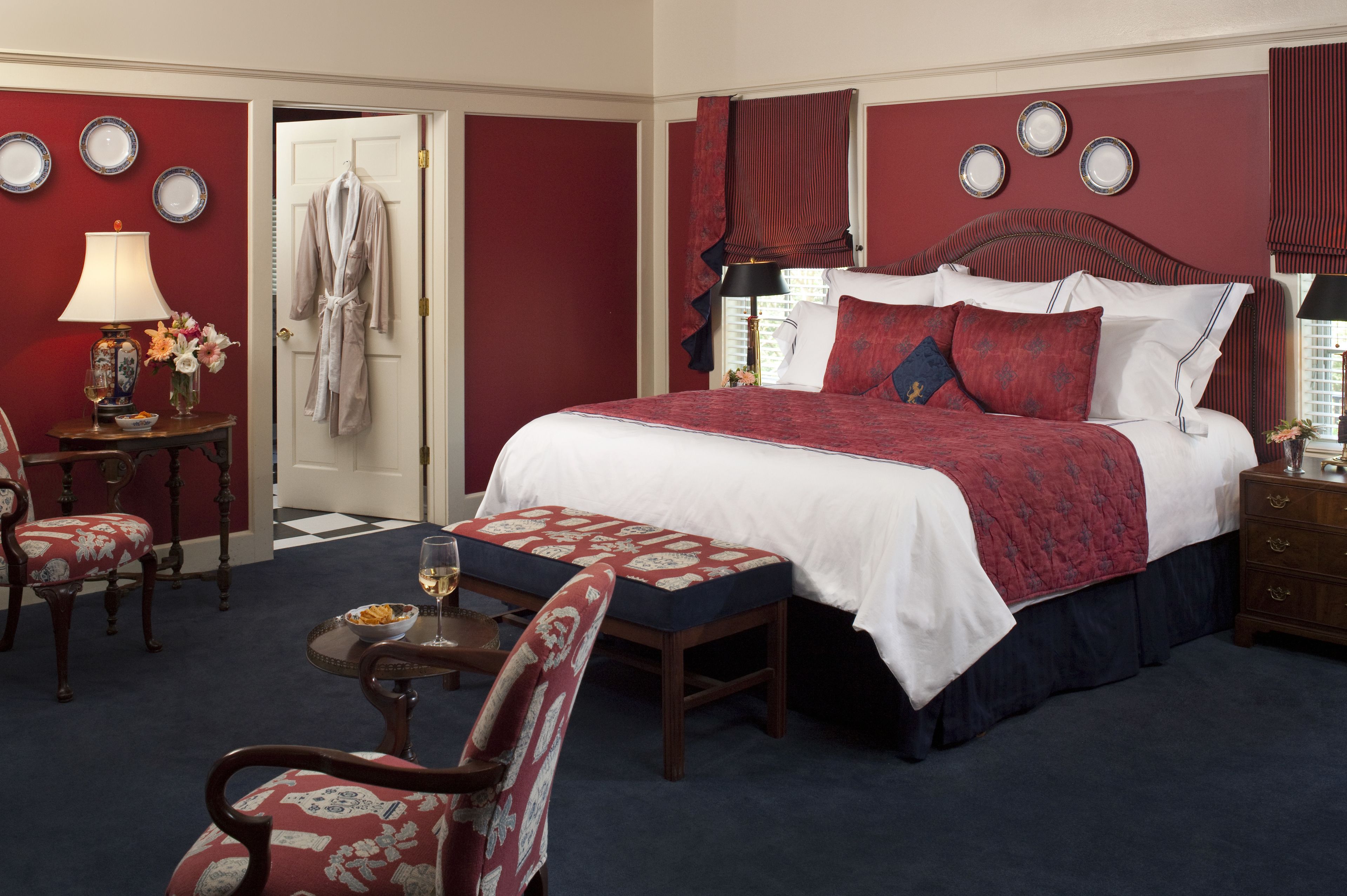 Une chambre d’hôtel avec un grand lit, un coin salon avec un fauteuil et une table, et une porte sur laquelle est accroché un peignoir.