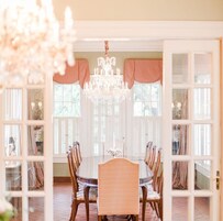 Un comedor con candelabro, sillas de madera y una mesa de vidrio.