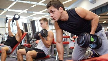 Un gimnasio con diferentes equipos de ejercicio y gente entrenando.