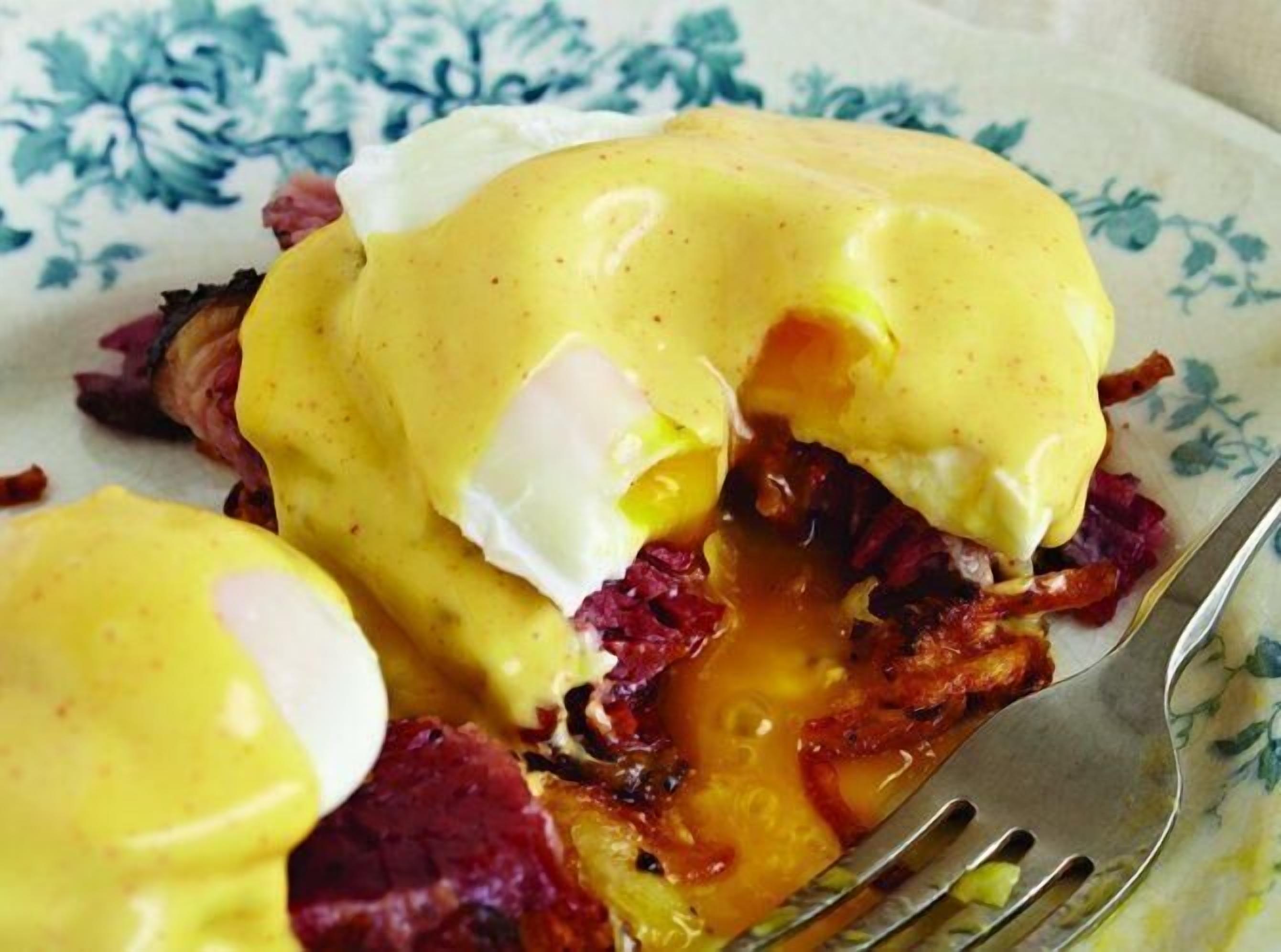 Primer plano de un plato de desayuno con huevos benedictinos sobre un plato con motivos florales.
