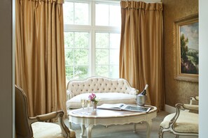 A room with a white tufted sofa, a round table with a champagne bottle, glasses, and a book, and two chairs.