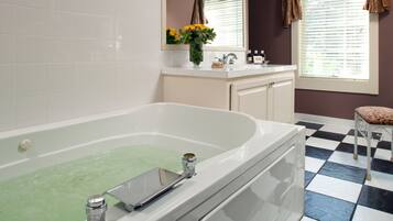 A bathroom with a large bathtub, a sink, and a window with curtains.