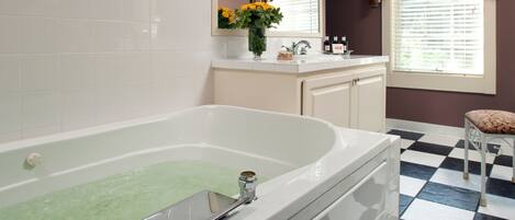 A bathroom with a large bathtub, a sink, and a window with curtains.