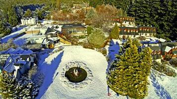 Paisagem coberta de neve com um edifício grande, uma estrutura circular e uma colina arborizada.