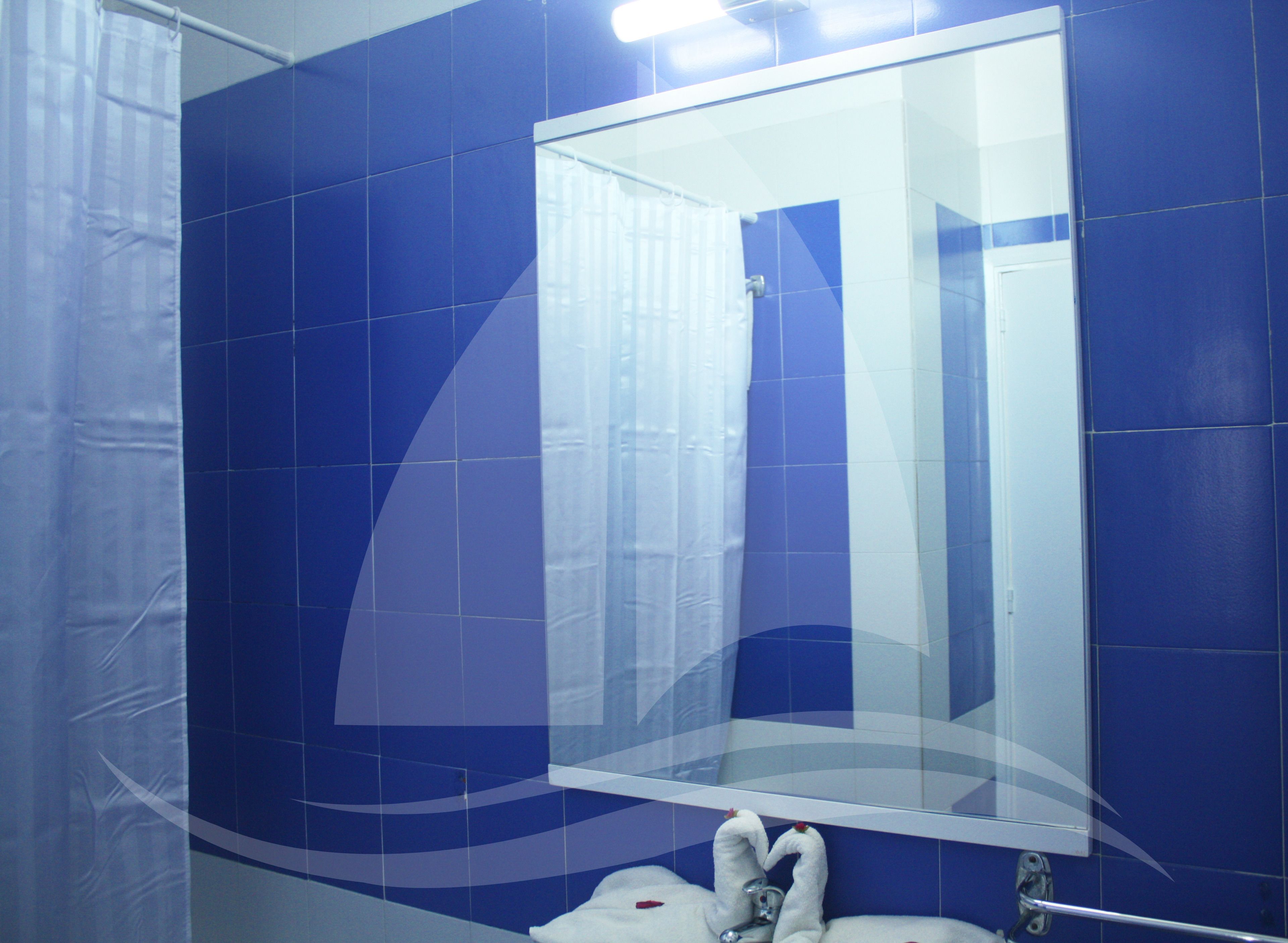 Un baño con azulejos azules, un espejo grande y una toalla blanca en el suelo.
