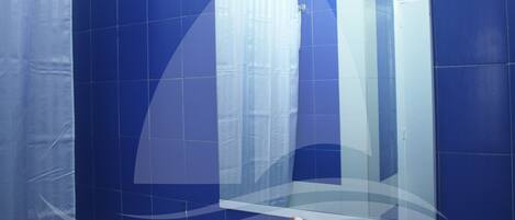Un baño con azulejos azules, un espejo grande y una toalla blanca en el suelo.