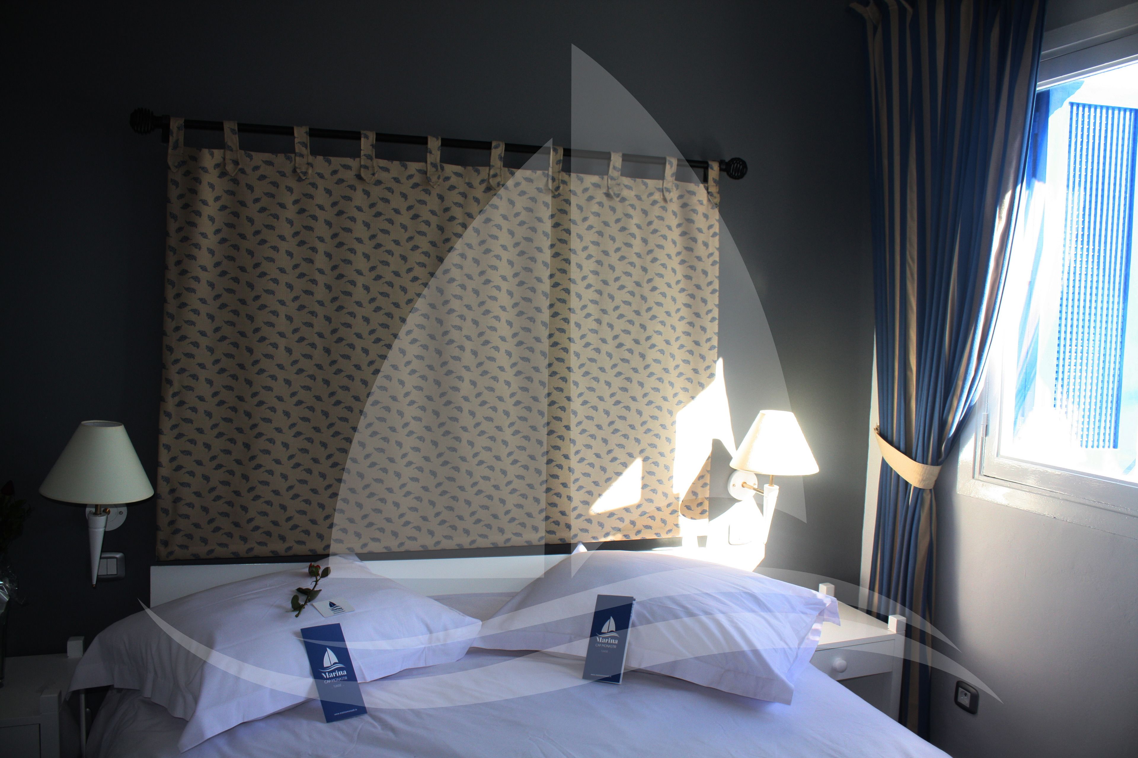 Ett hotellrum med en säng, gardiner och ett fönster.