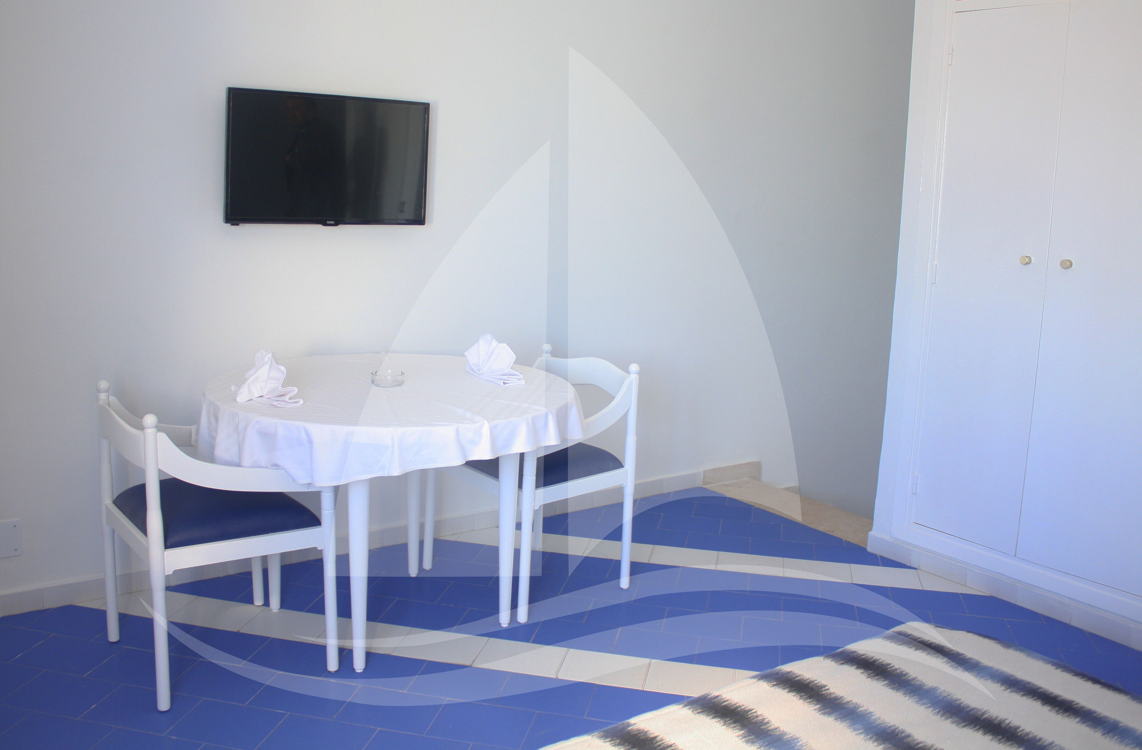 A room with a round table, two chairs, a flat-screen TV mounted on the wall, and a patterned rug on the floor.