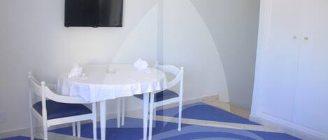 A room with a round table, two chairs, a flat-screen TV mounted on the wall, and a patterned rug on the floor.