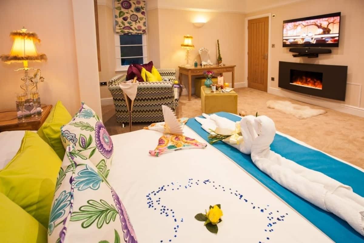 A hotel room with a bed, a sofa, a television, a fireplace, and a table with decorative items.