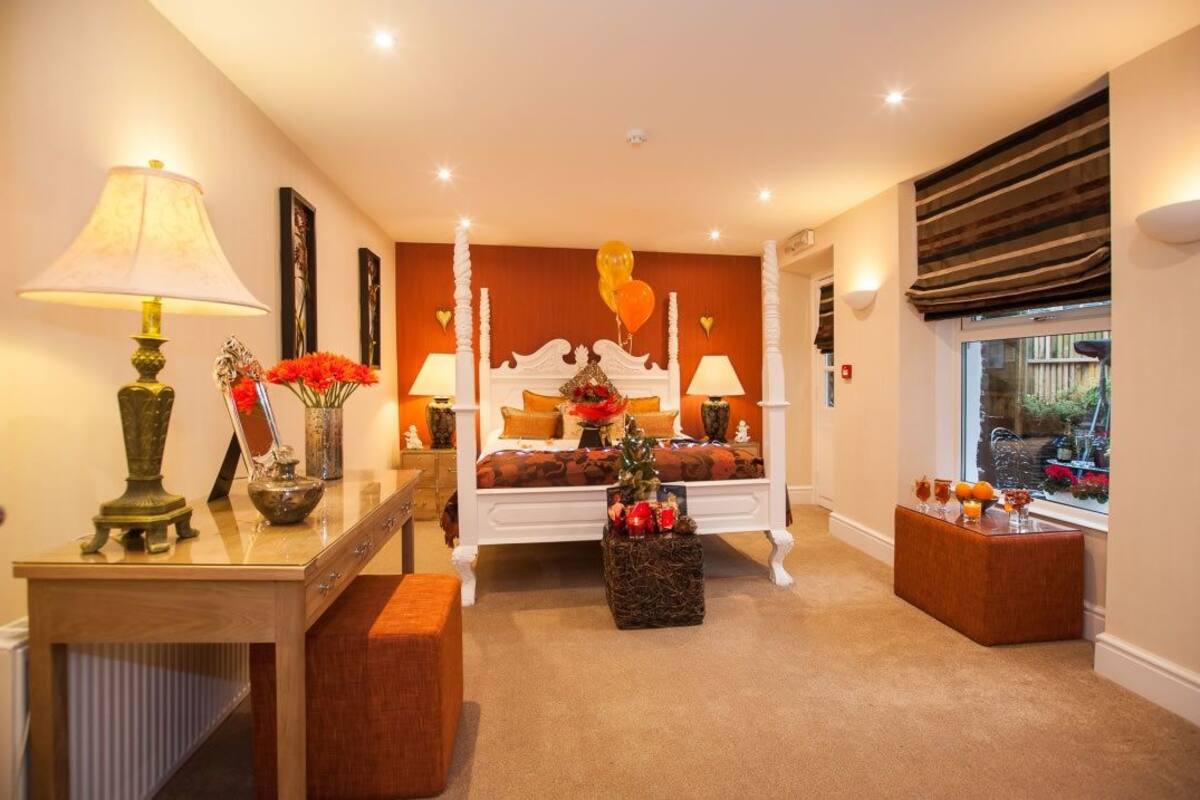 A bedroom with a bed, bedside lamps, a nightstand, a window with a view, and a decorative wall piece.