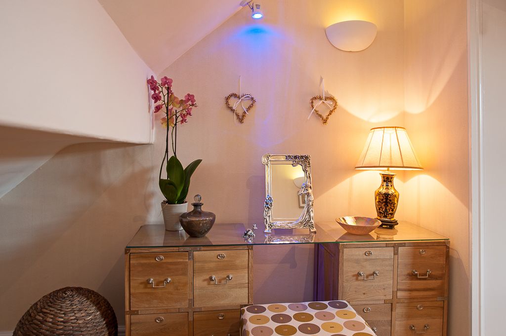 Un baño con tocador de vidrio, un espejo, una orquídea en maceta, un adorno con forma de corazón, una lámpara y un mantel con estampado.