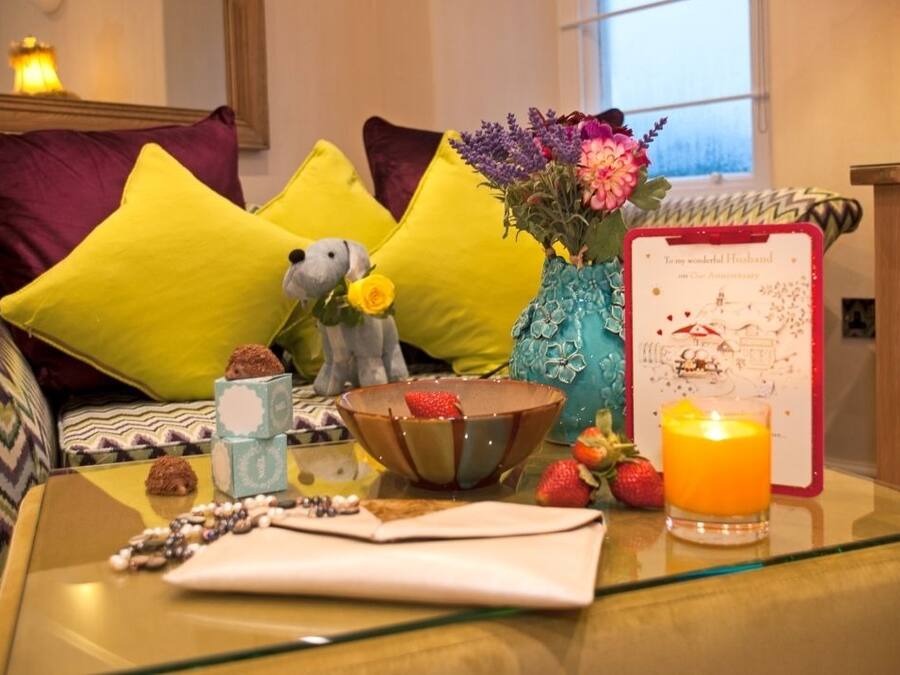 A cozy room with a sofa, pillows, a vase with flowers, a candle, and a framed card on a glass table.