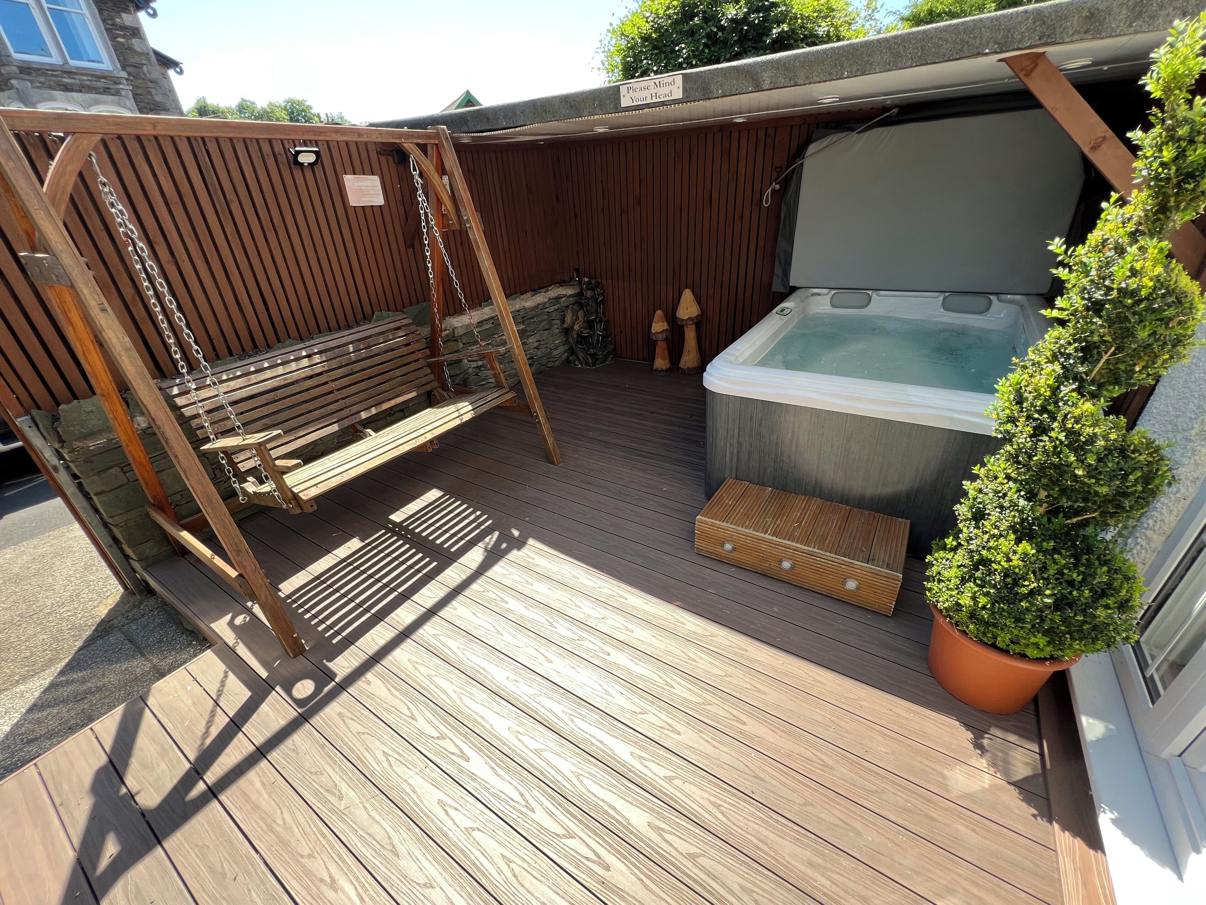 A wooden deck with a hot tub, a swing, and a potted plant.