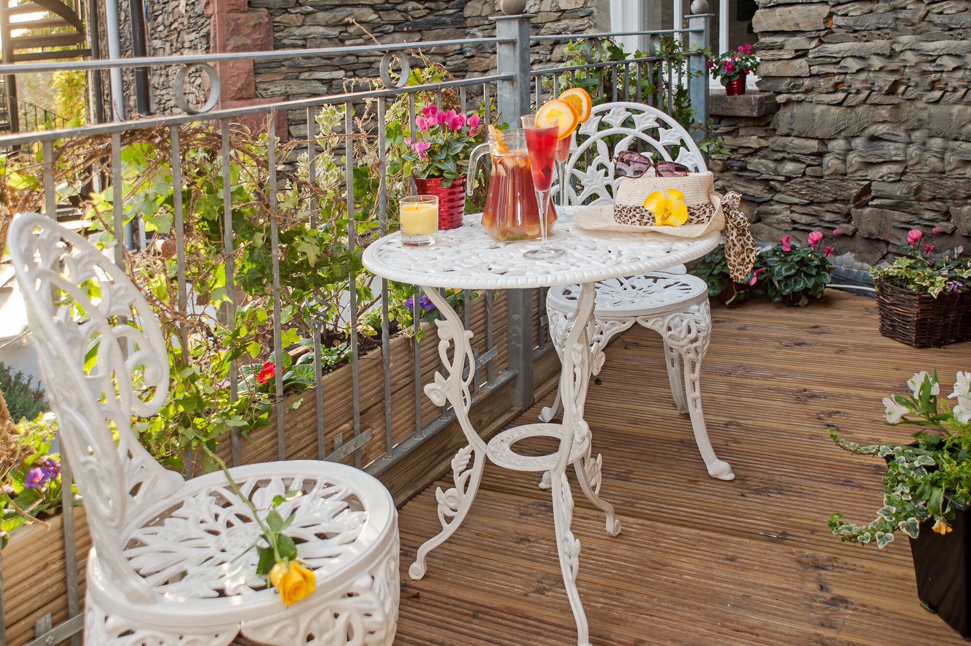 A white outdoor seating area with a table and chairs, surrounded by potted plants and flowers.