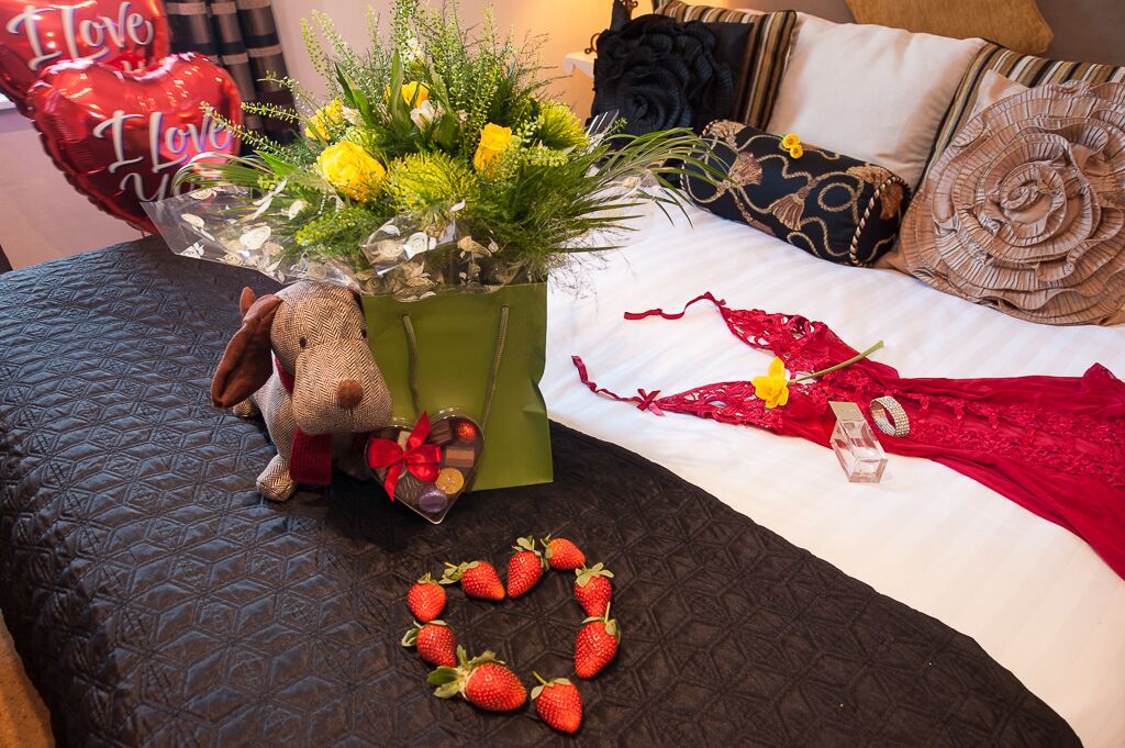 A bed with a bouquet of flowers, a teddy bear, and a heart-shaped arrangement of strawberries.