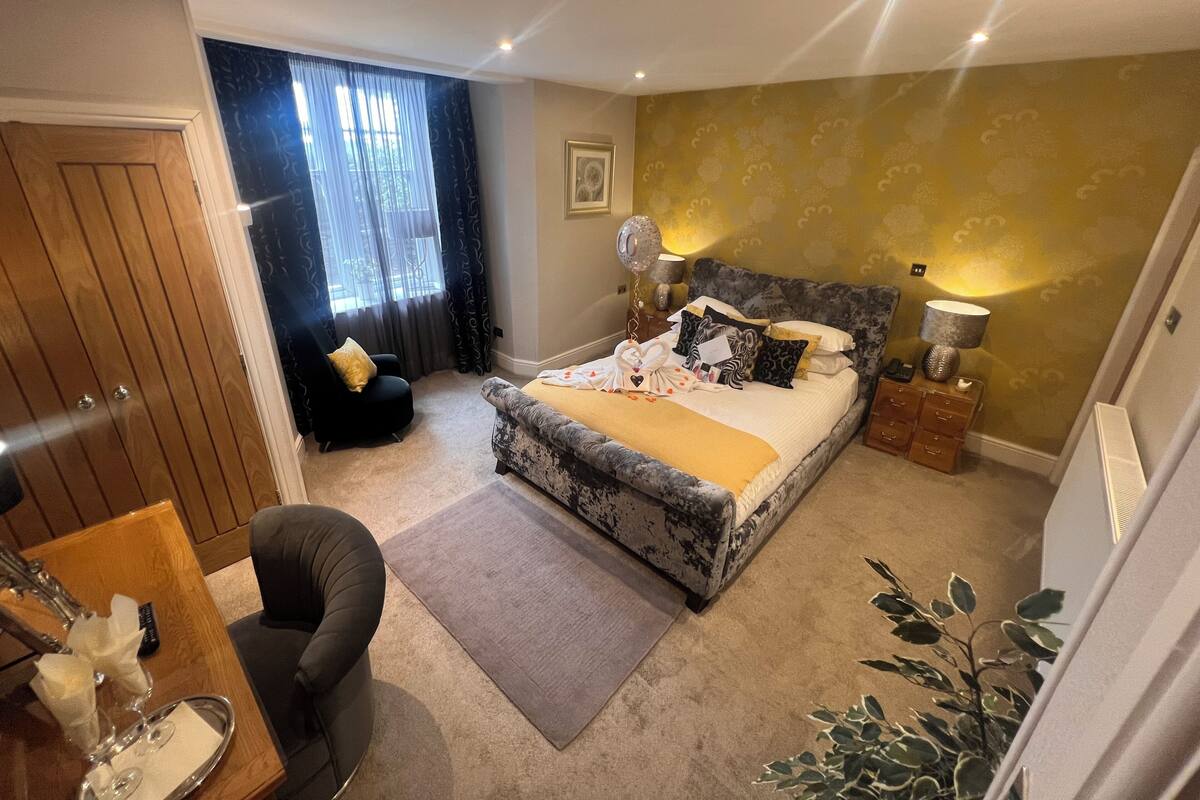 A bedroom with a bed, a chair, a bedside table, a lamp, and a plant.