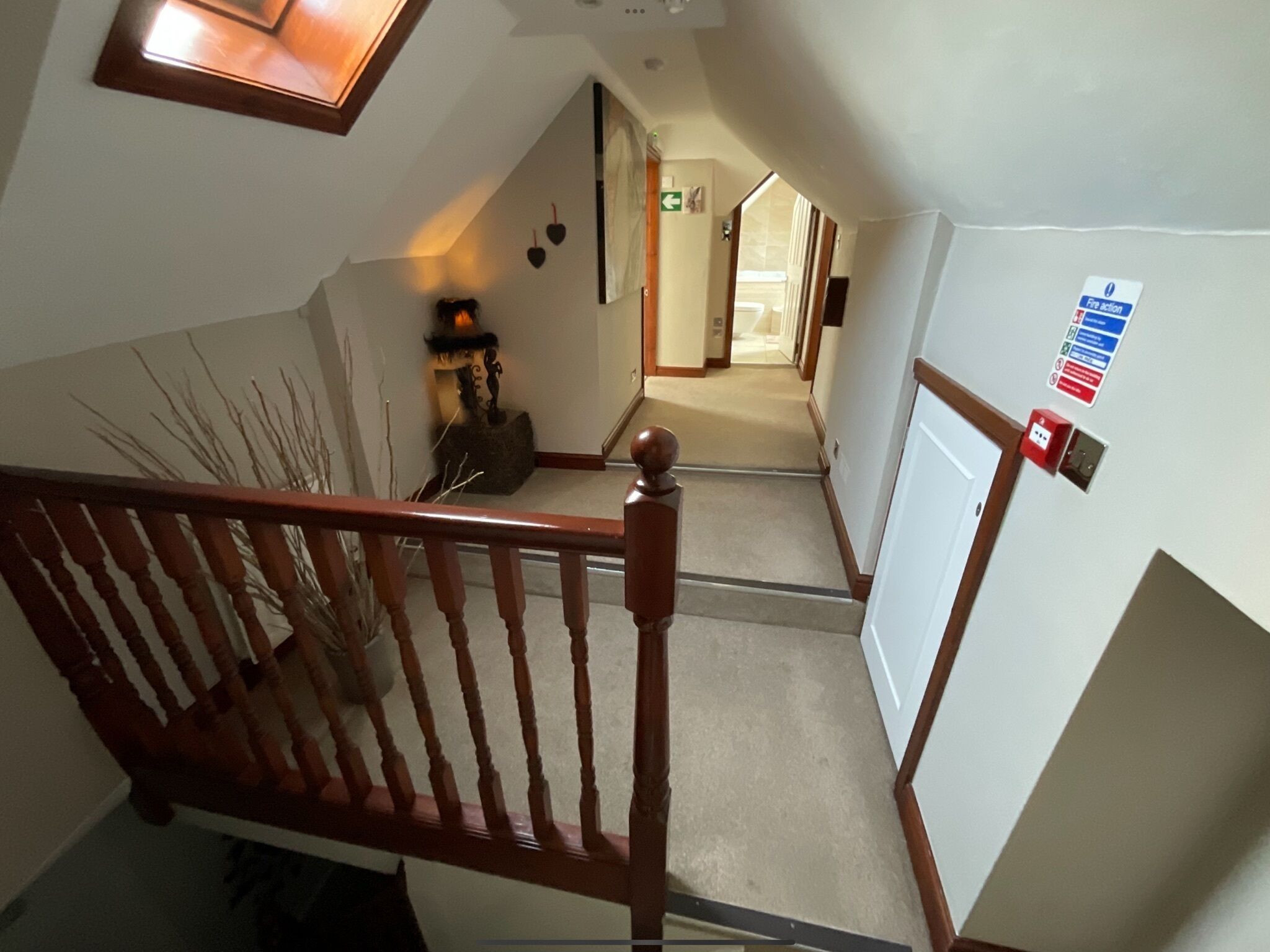 A staircase with a wooden handrail leading to a landing. A fire action sign is mounted on the wall to the right.