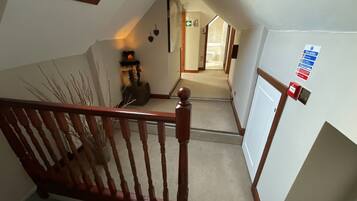 A staircase with a wooden handrail leading to a landing. A fire action sign is mounted on the wall to the right.