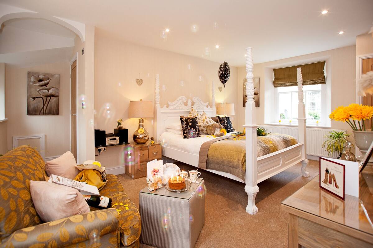 A bedroom with a four-poster bed, a sofa, a bedside table, and a window with a view.